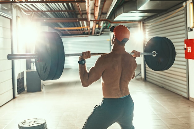 Il giovane uomo muscoloso sta facendo esercizi di snatch o shoulder press con bilanciere su un duro allenamento presso la palestra del garage.