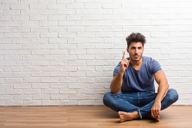 Il giovane uomo naturale si siede su un pavimento di legno che mostra il numero uno, simbolo di conteggio