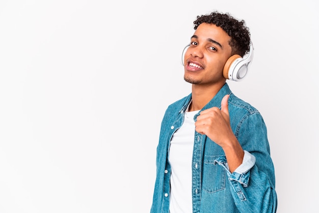 Il giovane uomo riccio afroamericano isolato ascoltando musica con le cuffie sorridendo e alzando il pollice