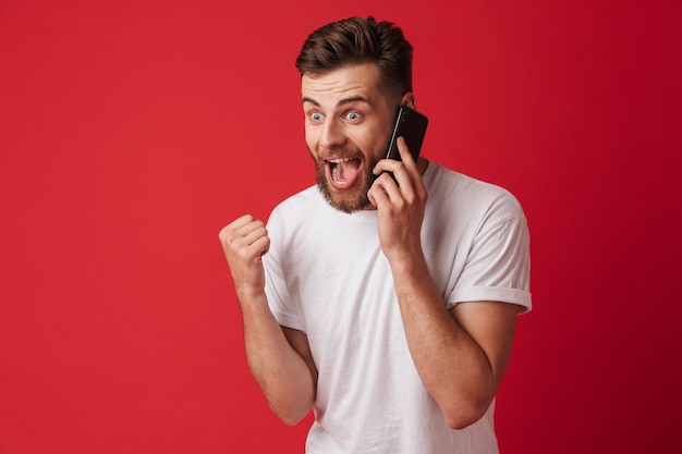 Il giovane uomo sorpreso bello che parla dal telefono cellulare fa il gesto del vincitore.