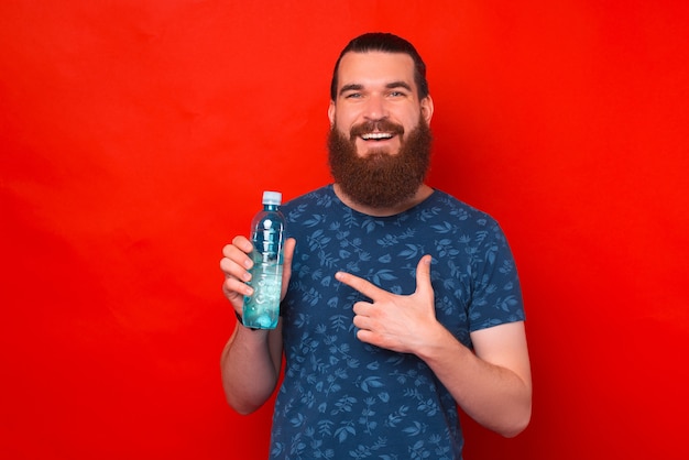 Il giovane uomo sorridente sta tenendo e indicando una bottiglia d'acqua.