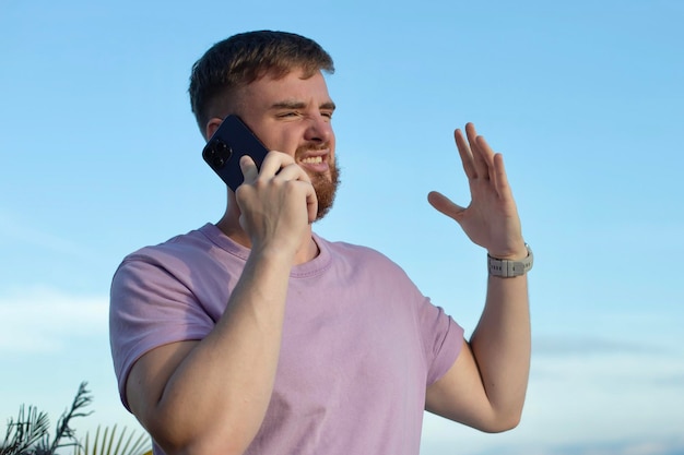 Il giovane uomo stressato arrabbiato e frustrato negativo sta parlando al cellulare chiamando lo smartphone litigando