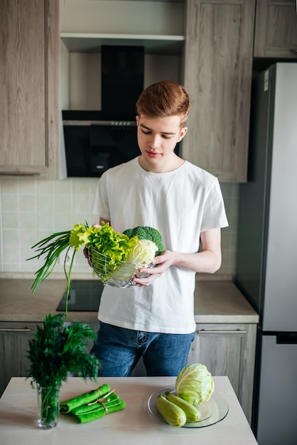 Il giovane uomo vegetariano sta cucinando l'insalata nella cucina dell'interno.