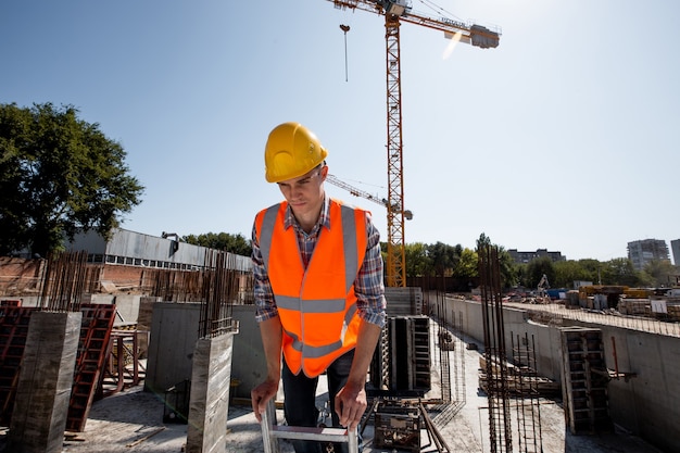 Il giovane vestito con camicia, giubbotto da lavoro arancione e casco lavora in cantiere.