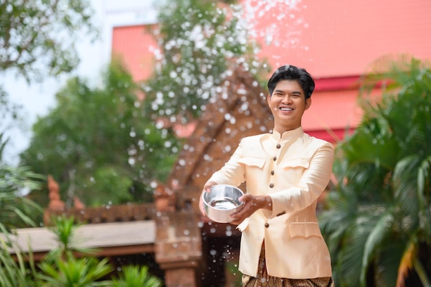 Il giovane vestito con splendidi costumi tailandesi si diverte a spruzzare acqua dalla ciotola nel tempio e preserva la buona cultura del popolo tailandese durante il festival di Songkran, il giorno della famiglia di Capodanno tailandese ad aprile