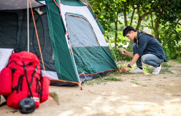 Il giovane viaggiatore usa una pietra per colpire i picchetti della tenda nella foresta durante il viaggio in campeggio durante le vacanze estive