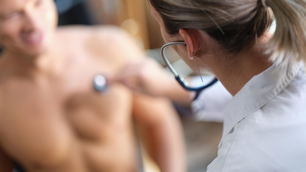 Il giovane viene in ospedale per il controllo sanitario medico femminile che usa lo stetoscopio per controllare il paziente