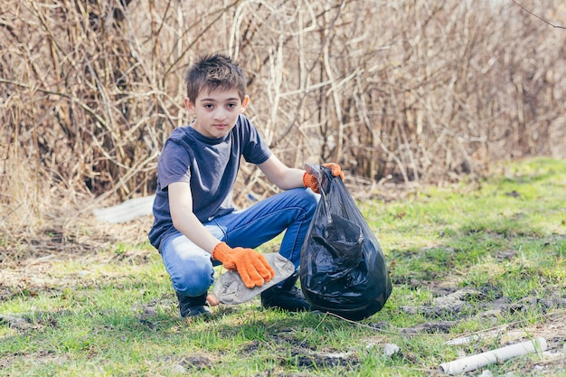 Il giovane volontario raccoglie la spazzatura nei boschi vestito con guanti arancioni mette le bottiglie di plastica in un sacco della spazzatura