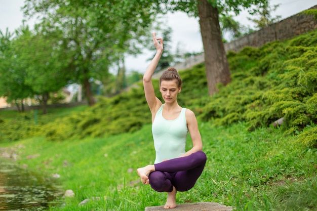 Il giovane Yogi castana snello si esercita complessa di yoga su erba verde.