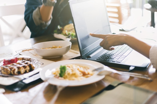 Il gruppo di amici è durante il pasto nel caffè. Ritaglia i giovani seduti al ristorante utilizzando il computer portatile.