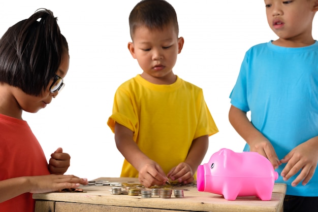 Il gruppo di bambini asiatici sta aiutando a mettere le monete nel porcellino salvadanaio isolato su fondo bianco