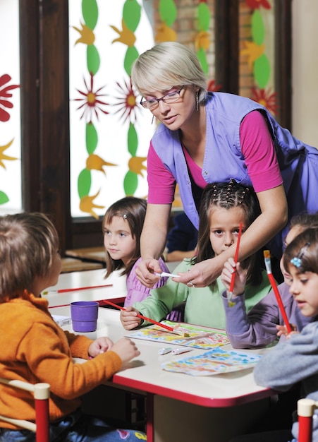 il gruppo di bambini felici si diverte e gioca al concetto di educazione prescolare al coperto dell'asilo con l'insegnante