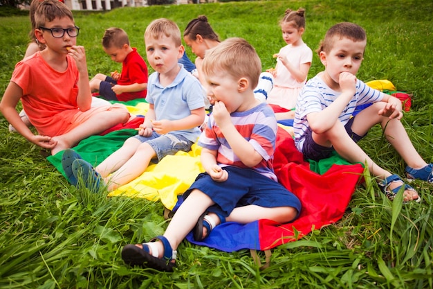 Il gruppo di bambini in età prescolare fa uno spuntino nel parco I bambini sono seduti sul copriletto e mangiano i biscotti