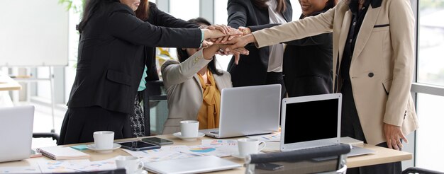 Il gruppo di donna d'affari di successo femminile irriconoscibile non identificata in affari casuali indossa in piedi tenendosi per mano insieme potenziare come accordo di impegno di partnership di lavoro di squadra nell'ufficio dell'azienda.