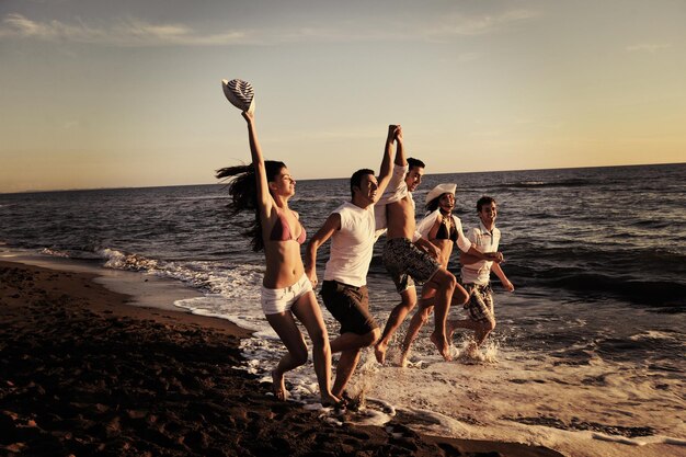 il gruppo di giovani felici si diverte a correre e saltare su beacz all'ora del tramonto