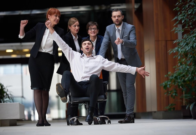 il gruppo di uomini d'affari in un ufficio moderno al chiuso si diverte e spinge la sedia da ufficio sul corridoio