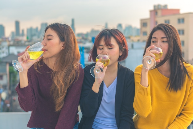 Il gruppo felice di ragazze asiatiche gode della risata e del bicchiere di vino spumante allegro alla festa sul tetto