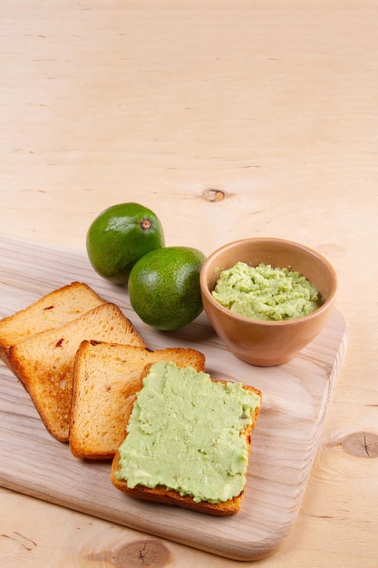 Il guacamole adorna il pane al pomodoro tostato su tagliere di legno e frutti di avocado Banner verticale