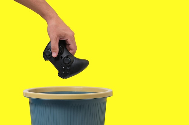 Il joystick del gioco viene gettato nel cestino su sfondo giallo. Concetto di abbandono dei giochi per computer.