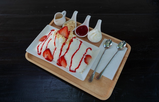 Il kakigori alla fragola (sapore di latte da dessert con ghiaccio tritato giapponese) o il bingsu (dessert della Corea) servono su un piatto bianco con salsa di fragole e condimenti sul tavolo, cibo dolce