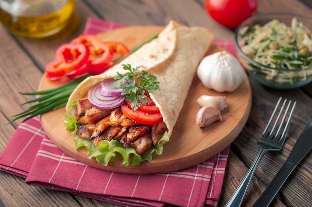 Il kebab di Doner giace sul tagliere. Shawarma con carne di pollo, cipolle, insalata si trova su un vecchio tavolo di legno scuro.