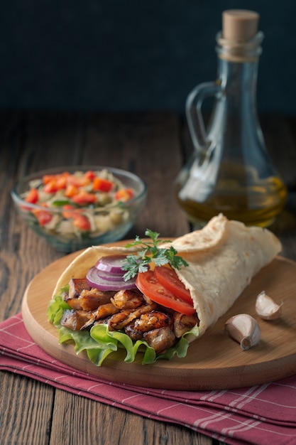 Il kebab di Doner giace sul tagliere. Shawarma con carne di pollo, cipolle, insalata si trova su un vecchio tavolo di legno scuro.