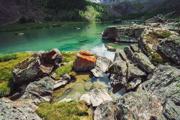 Il lago di montagna è circondato da grandi pietre e massi con muschi