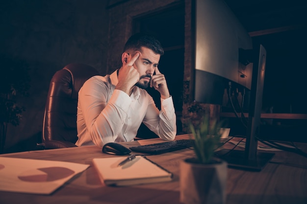 Il lato del profilo dell'uomo concentrato si siede le tempie delle dita del pc del computer del lavoro della tavola