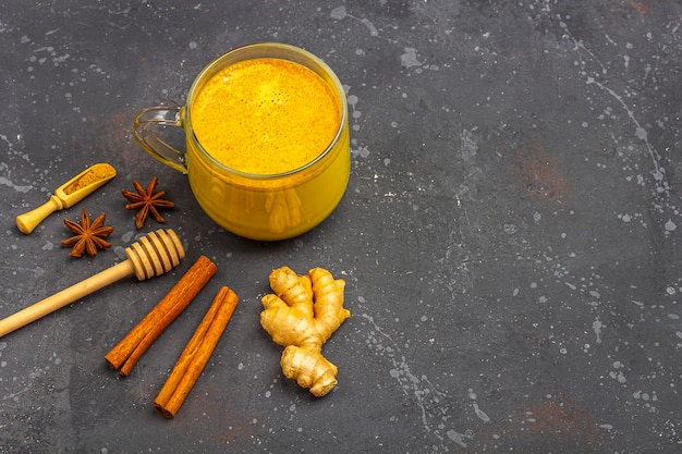 Il latte di curcuma della bevanda indiana tradizionale è latte dorato in tazza di vetro con cannella, la stella dell'anice, curcuma su fondo scuro. Perdita di peso, bevanda sana e biologica