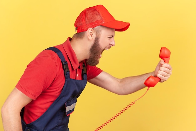 Il lavoratore aggressivo che indossa una tuta blu che urla al cliente sul telefono non accetta l'ordine
