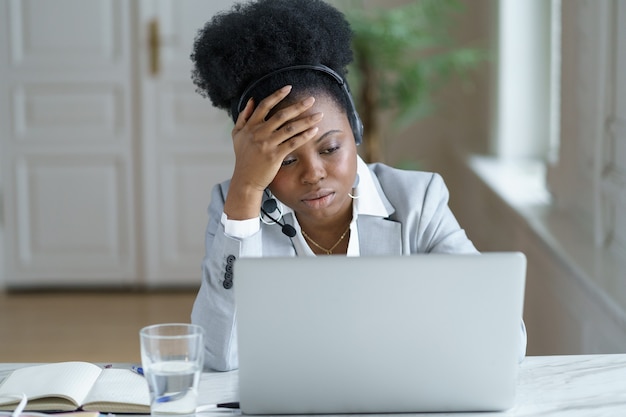Il lavoratore del call center di supporto femminile africano stanco in cuffia sembra frustrato arrabbiato sullo schermo del laptop