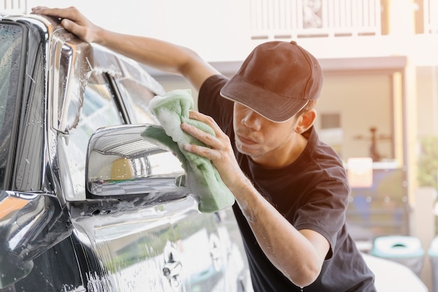 Il lavoratore dell&#39;autolavaggio che indossa una maglietta e un berretto nero utilizza una spugna per pulire l&#39;auto.