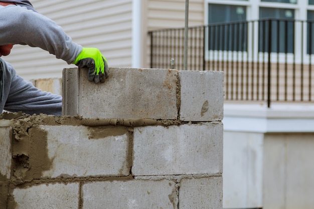 Il lavoratore della massoneria fa il muro di cemento dal blocco e dall&#39;intonaco del cemento al cantiere