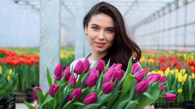 Il lavoratore della serra della giovane bella donna tiene una scatola con i tulipani in fiore nelle sue mani e sorride