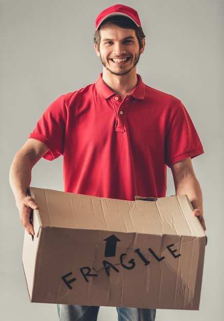 Il lavoratore delle consegne in uniforme rossa sta tenendo una scatola di cartone.