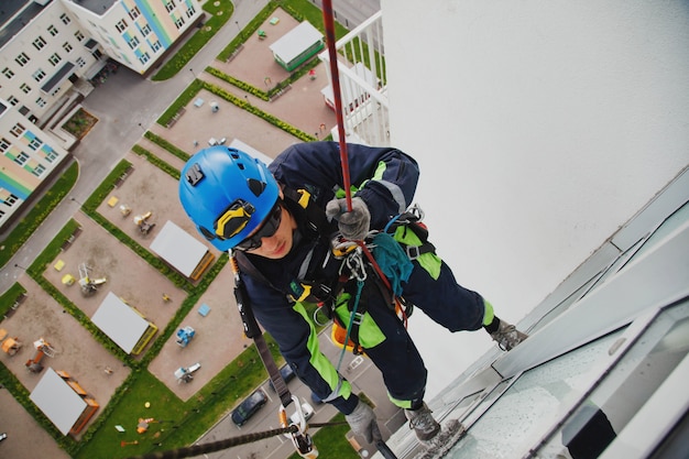 Il lavoratore di alpinismo industriale pende sopra l'edificio della facciata residenziale mentre lava i vetri della facciata esterna. L'addetto alla fune è appeso al muro della casa. Concetto di opere urbane. Copia spazio per il sito