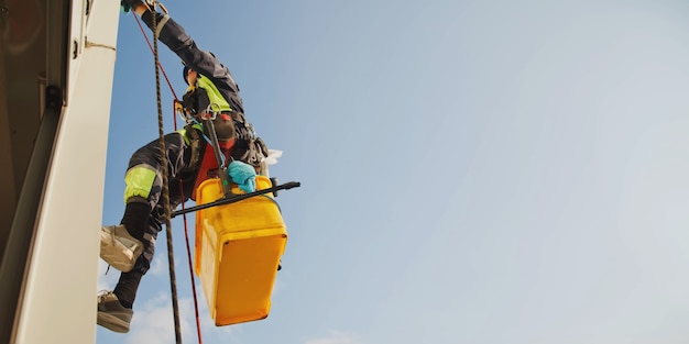 Il lavoratore di alpinismo industriale pende sopra l'edificio della facciata residenziale mentre lava i vetri della facciata esterna. L'addetto alla fune è appeso al muro della casa. Concetto di opere urbane. Copia spazio per il sito