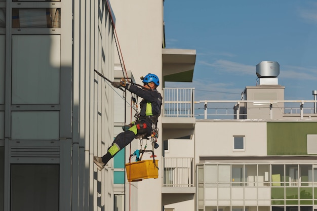 Il lavoratore di alpinismo industriale pende sopra l'edificio della facciata residenziale mentre lava i vetri della facciata esterna. L'addetto alla fune è appeso al muro della casa. Concetto di opere urbane. Copia spazio per il sito