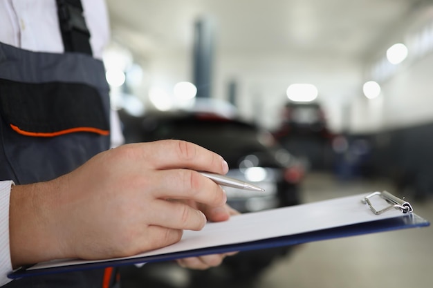 Il lavoratore di servizio maschio riempie la documentazione di manutenzione dopo aver riparato l'auto