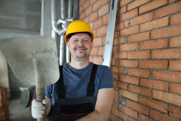 Il lavoratore in cappello duro tiene la pala del cemento