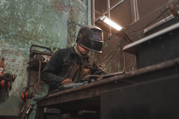 Il lavoratore in una maschera del saldatore lavora in un'officina per saldare il ferro.