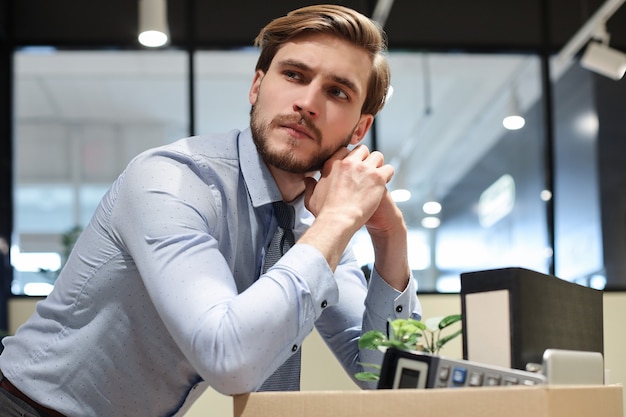 Il lavoratore licenziato triste sta portando con sé le sue forniture per ufficio dall'ufficio.