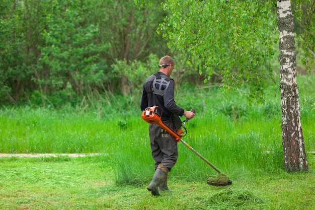 Il lavoratore maschio falcia l'erba sullo sfondo della foresta