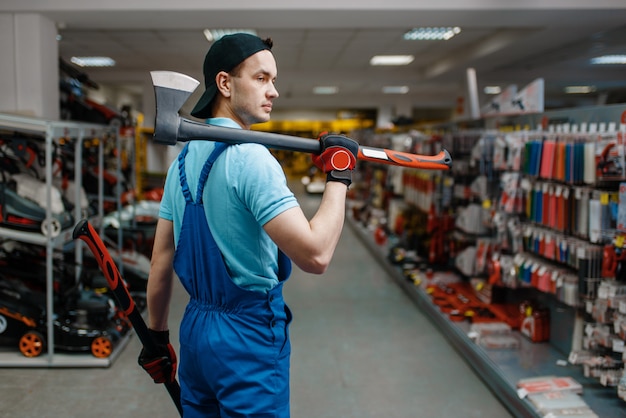 Il lavoratore maschio in uniforme tiene due assi, deposito degli attrezzi