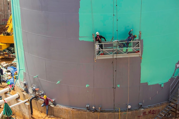 Il lavoratore maschio prende la funivia tenendo in mano una spazzola per pittura industriale utilizzata per il colore verde della superficie della superficie dell'olio del serbatoio della piastra delle coperture