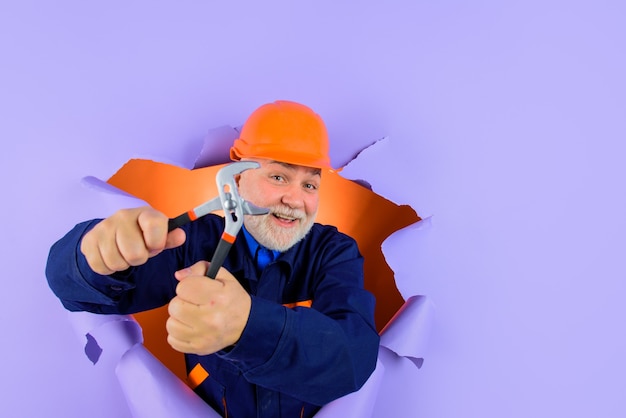 Il lavoratore o il costruttore in casco con le pinze che guardano attraverso l'idraulico professionista di carta tiene le pinze auto