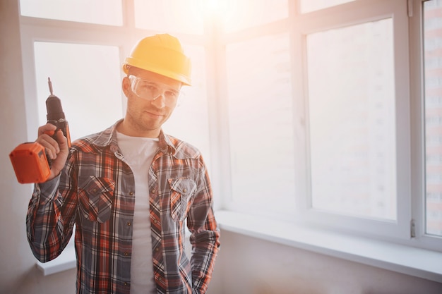 Il lavoratore o il costruttore tiene un trapano elettrico. Concetto di costruzione o riparazione. Sullo sfondo della costruzione