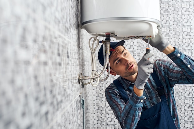 Il lavoratore quasi finito ha installato la caldaia per il riscaldamento elettrico nel bagno di casa