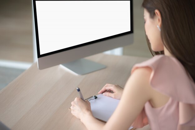 Il lavoratore sta scrivendo e guardando lo schermo del computer. Sta lavorando al tavolo