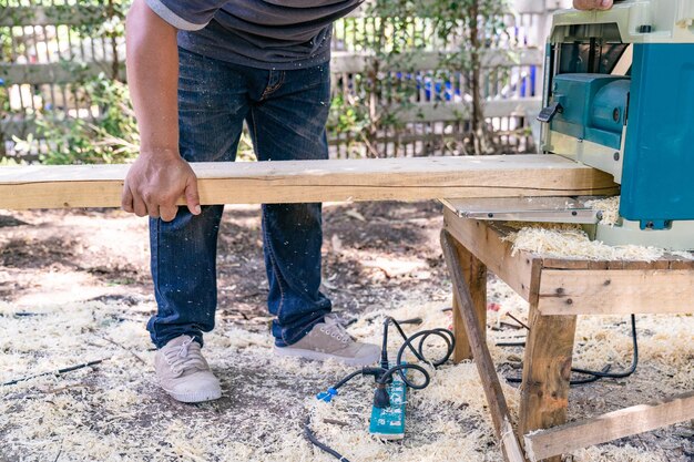 Il lavoratore strofina il grande piatto di legno lungo con la lucidatrice in giardino